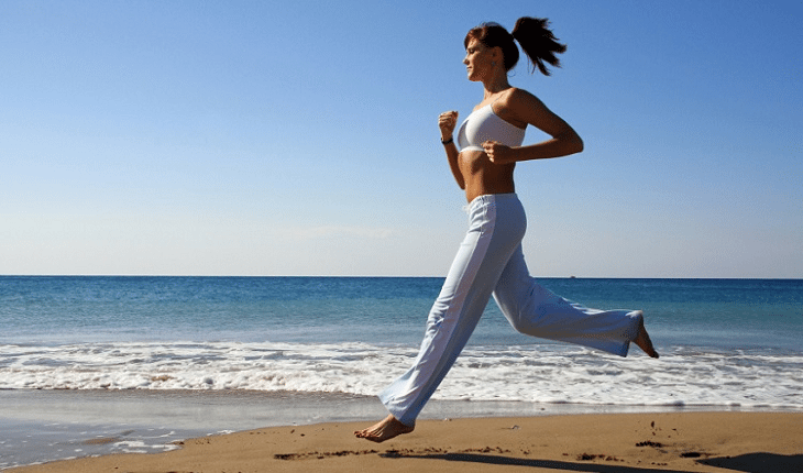 Mulher com roupa branca correndo na beira do mar