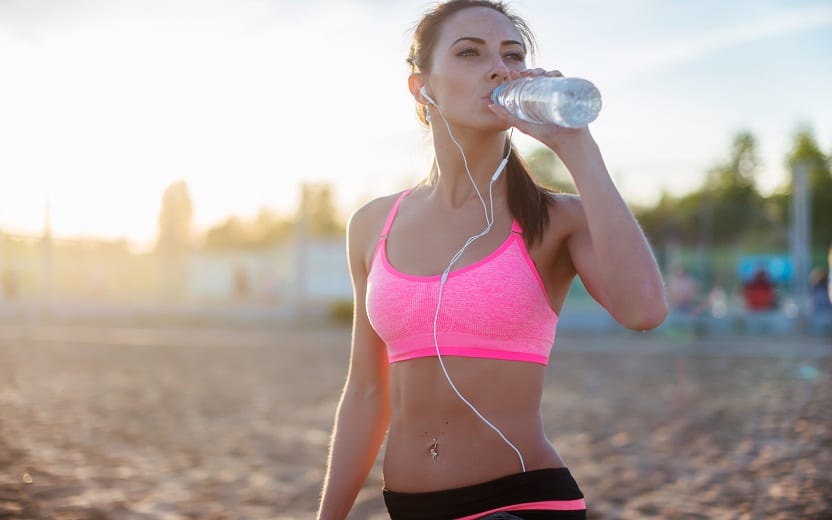 mulher em uma praia usando fones de ouvido e bebendo água tomar água