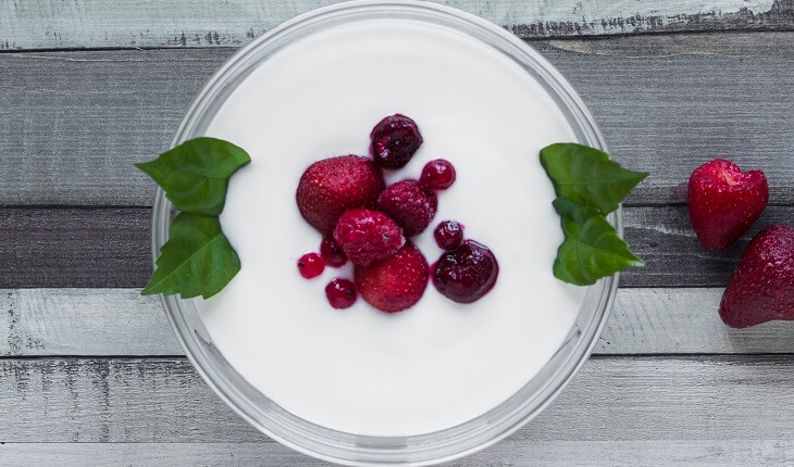 Ingestão de proteínas: na foto, uma foto de um copo de iogurte com frutas vermelhas visto de cima.