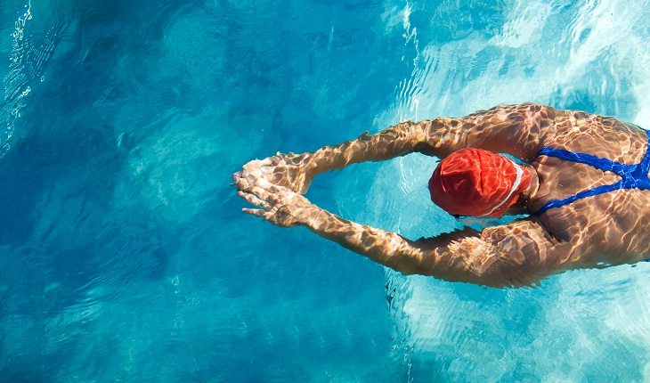 Atividades físicas indicadas para pessoas com hemofilia: natação. Na foto, uma pessoa vista de cima em uma piscina, nadando.