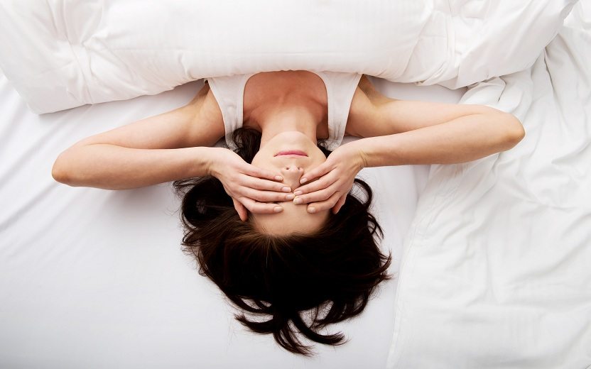 Mulher deitada em cama com mãos no rosto evitar antes de dormir