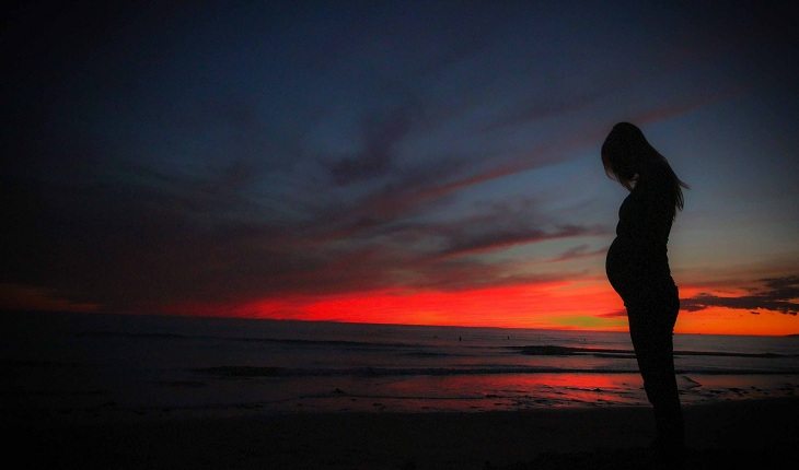 Mulher grávida sob o por do sol de uma praia corrida durante a gravidez
