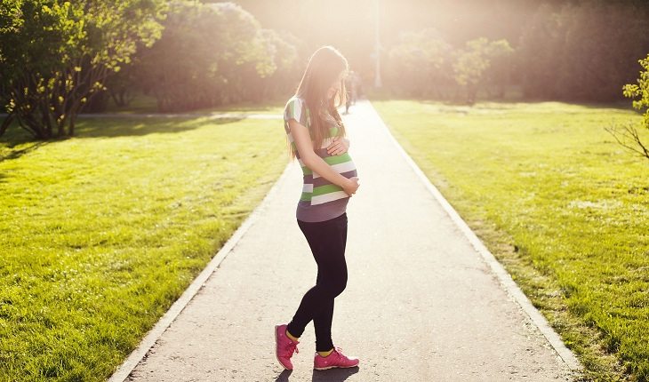 Mulher grávida em uma trilha segurando sua barriga corrida durante a gravidez