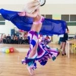 Uma mulher com as vestimentas roxas rodopia em uma aula de dança do vente