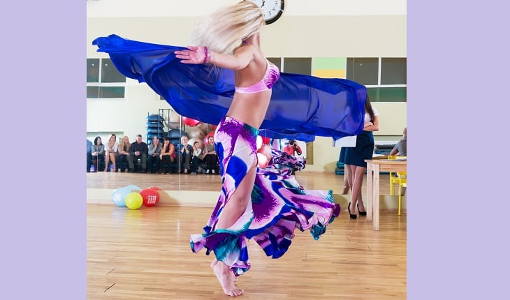 Uma mulher com as vestimentas roxas rodopia em uma aula de dança do vente