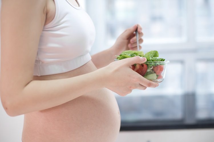 Alimentação na gravidez. Foto que mostra a barriga de uma mulher grávida, enquanto ela come salada