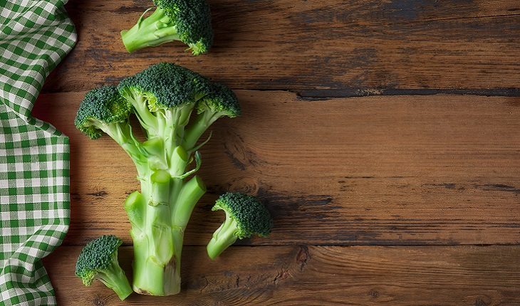 A foto mostra pedaços de brócolis, um dos alimentos antienvelhecimento, em cima de uma mesa de madeira ao lado de uma toalha quadriculada verde e branca