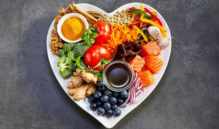 Prevenção do câncer: alimentação balanceada. Na foto, um prato em formato de coração com frutas, verduras, legumes, peixes, dentre outros alimentos.