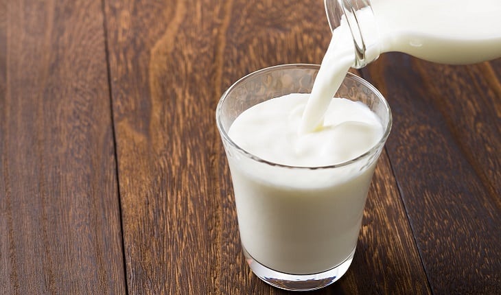 A foto mostra uma pessoa derramando leite de uma garrafa em um copo, um dos alimentos para corredores