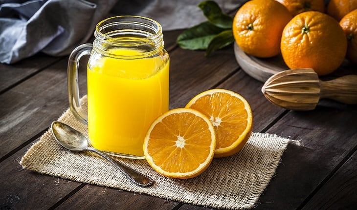 A foto mostra uma laranja partida ao meio ao lado de um copo com suco de laranja, um dos alimentos para corredores
