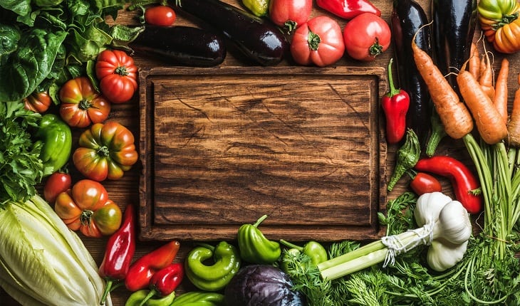 A foto mostra vegetais e legumes variados ao redor de uma tábua de madeira. Esses são indicações de alimentos para corredores