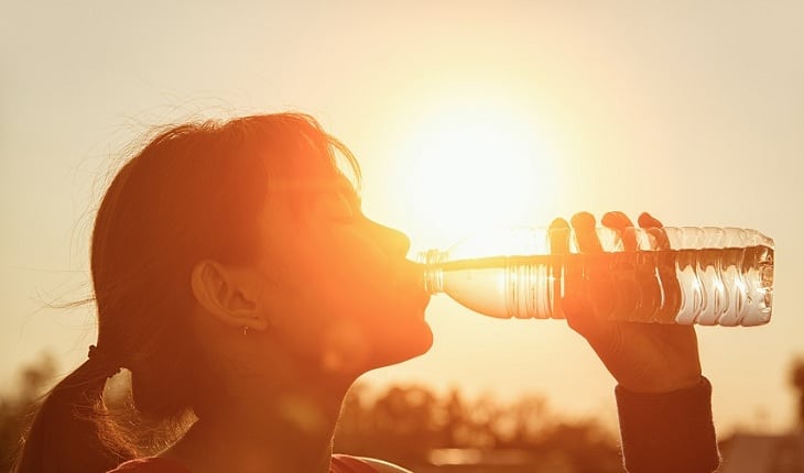 Mulher bebendo água no por do sol, seguindo os conselhos de especialistas, hidrate-se