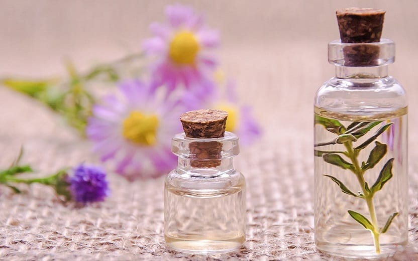 A foto mostra dois frascos, um grande e um pequeno com óleos aromáticos e flores ao fundo, ilustrando o tema do post sobre os benefícios da aromaterapia
