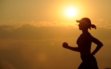 Silhueta de uma mulher correndo durante o dia. Benefícios do exercício contra o câncer