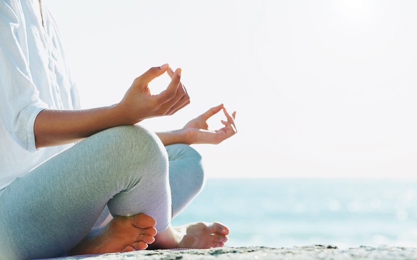 Pessoa sentada em uma praia com o mar ao fundo, prestando atenção e aprendendo a meditar em um passo a passo