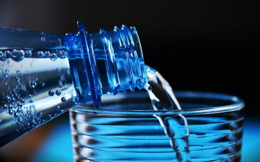 Dicas para evitar pedras nos rins: beber água. Na imagem, uma garrafa enchendo copo de água.
