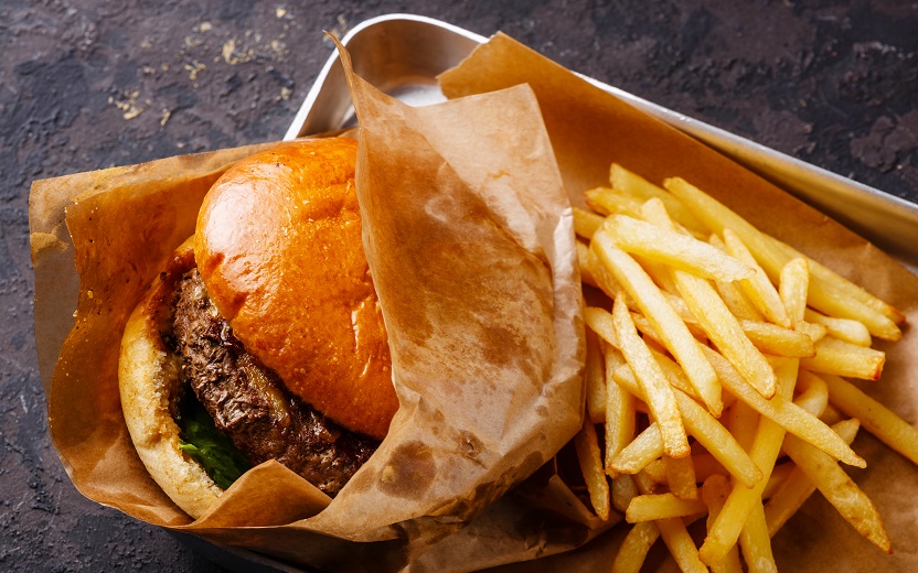 Pão com hambúrguer e batata fritas em embalagens. Nutrientes são ricos em gorduras e fazem parte da categoria comfort food