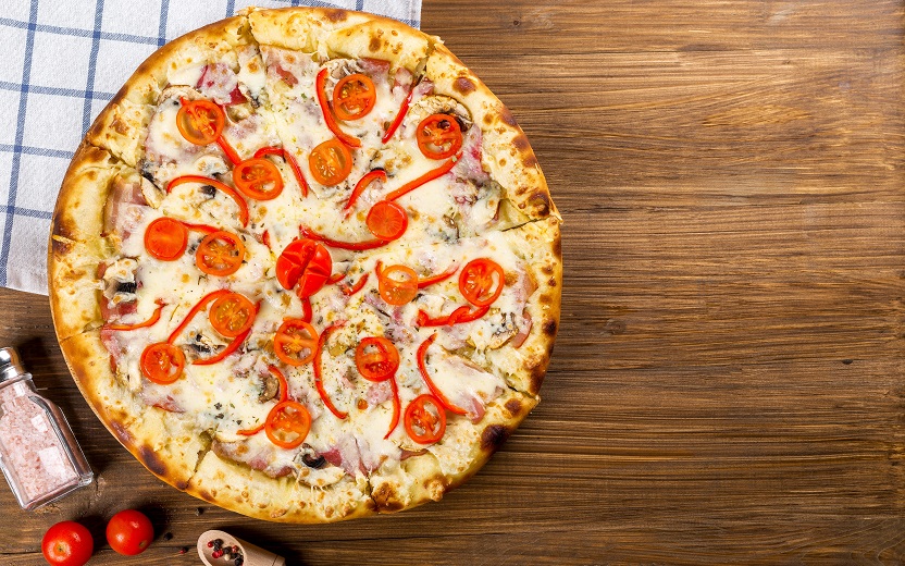 Pizza em cima de um balcão de madeira. Contém queijo mussarela, tomate e azeitona. Nutriente é um comfort food