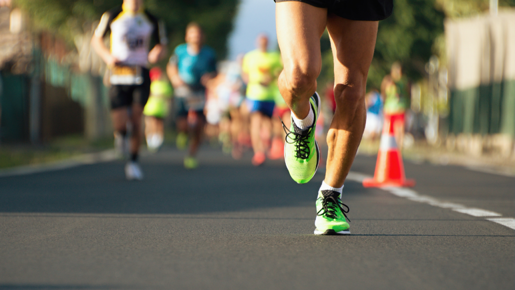 Grupo de corredores participando de uma maratona, atravessando a cidade em ritmo competitivo durante o dia.