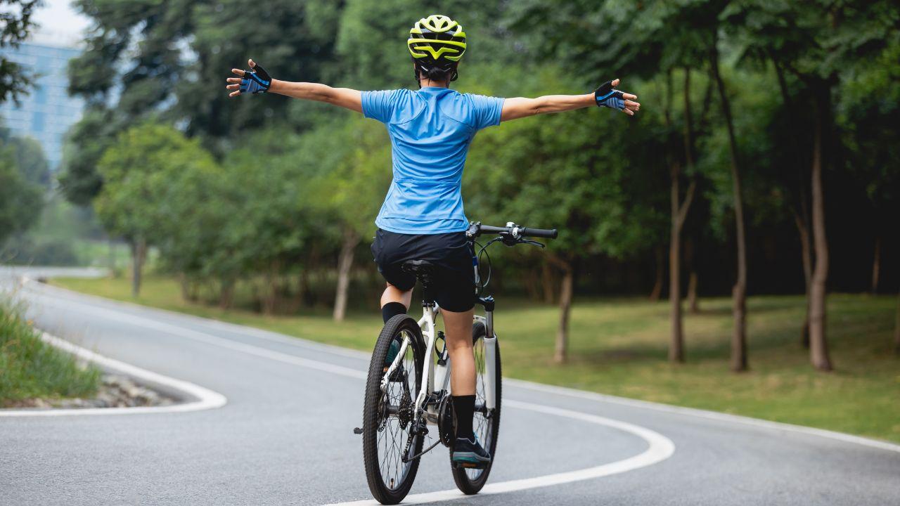 Mulher ciclista, usando roupa azul andando de bicicleta na estrada.
