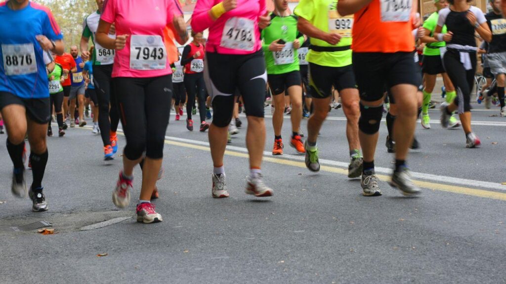 Pessoas correndo na rua usando coletes coloridos em uma corrida.