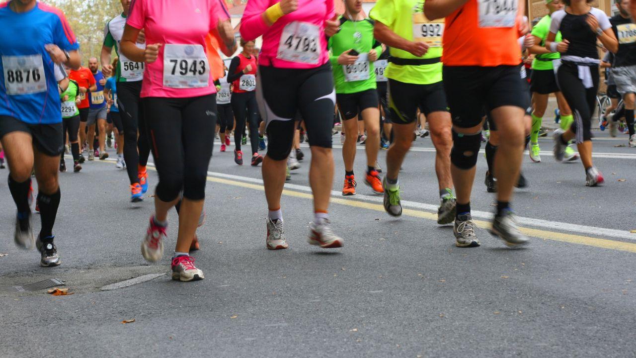 Pessoas correndo na rua usando coletes coloridos em uma corrida.