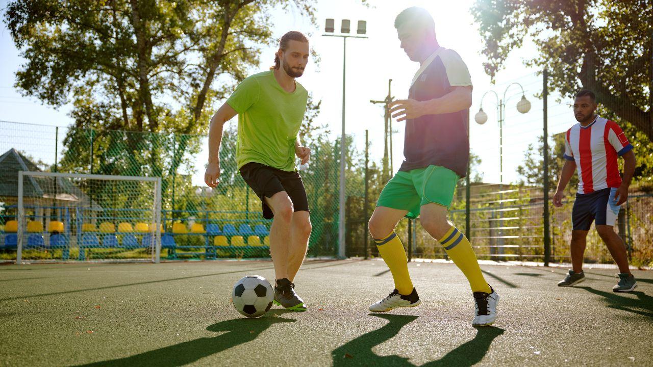 Homens jogando bola de futebol em uma quadra de bairro.