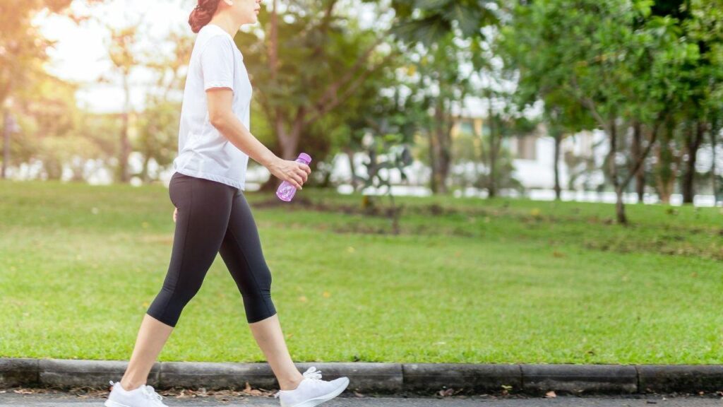 Mulher com camiseta branca e legging preta caminhando em um parque.
