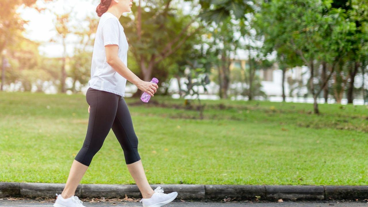Mulher com camiseta branca e legging preta caminhando em um parque.