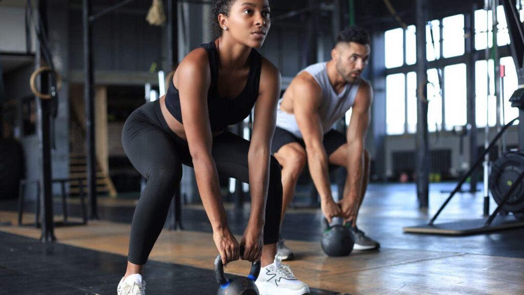 Mulher negra e homem branco levantando peso na academia.