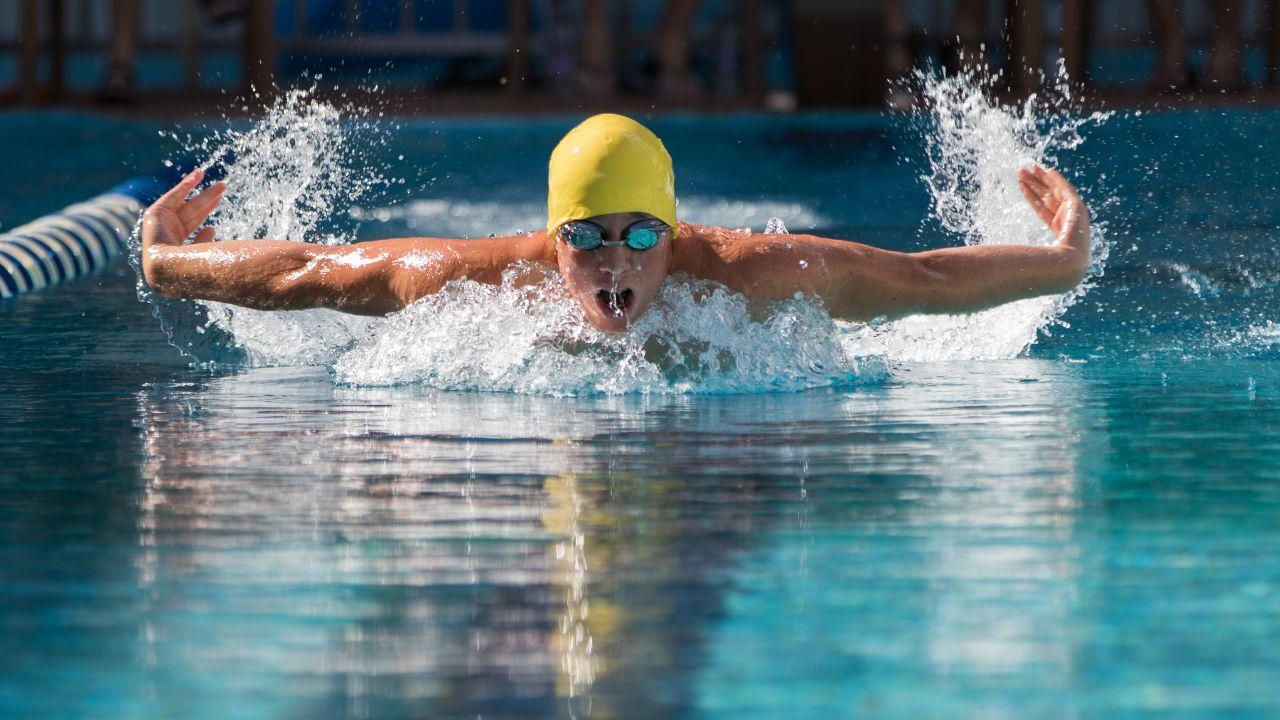 Homem branco dentro da piscina nadando com touca e óculos de mergulho dando braçadas de natação.
