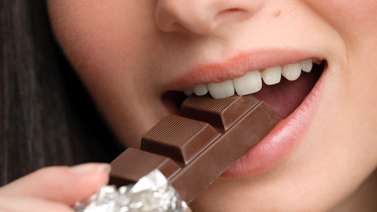 Imagem de uma mulher mordendo uma barra pequena de chocolate