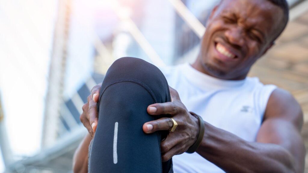Imagem de um homem segurando o joelho, com roupa de corrida e cara de dor
