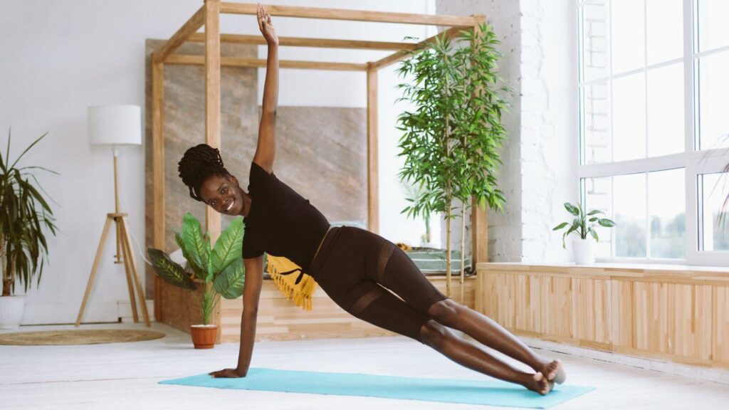 Imagem de uma mulher fazendo prancha lateral em cima de um tapete de yoga azul claro