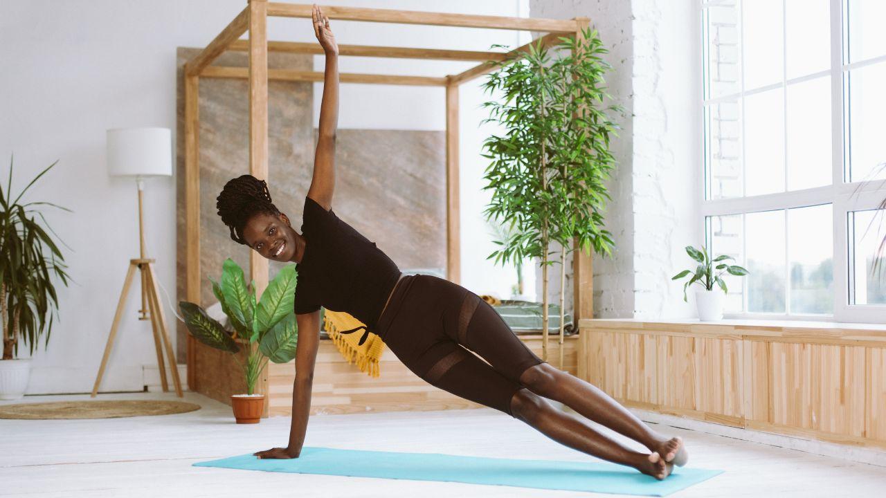 Imagem de uma mulher fazendo prancha lateral em cima de um tapete de yoga azul claro