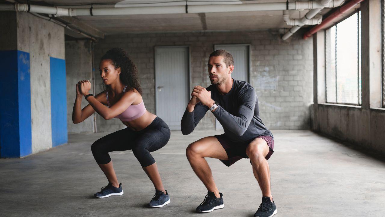 Mulher e homem fazendo agachamentos na academia.