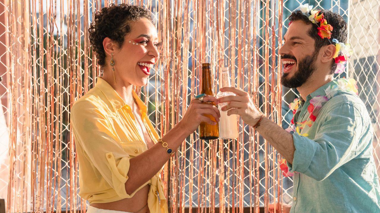 Mulher e homem brindando duas garrafas de cerveja.