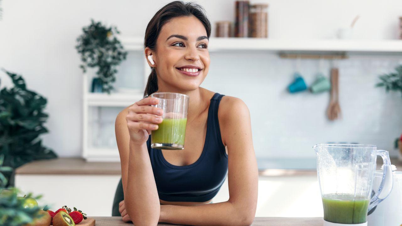 Mulher escorada na bancada segurando um copo de suco verde.