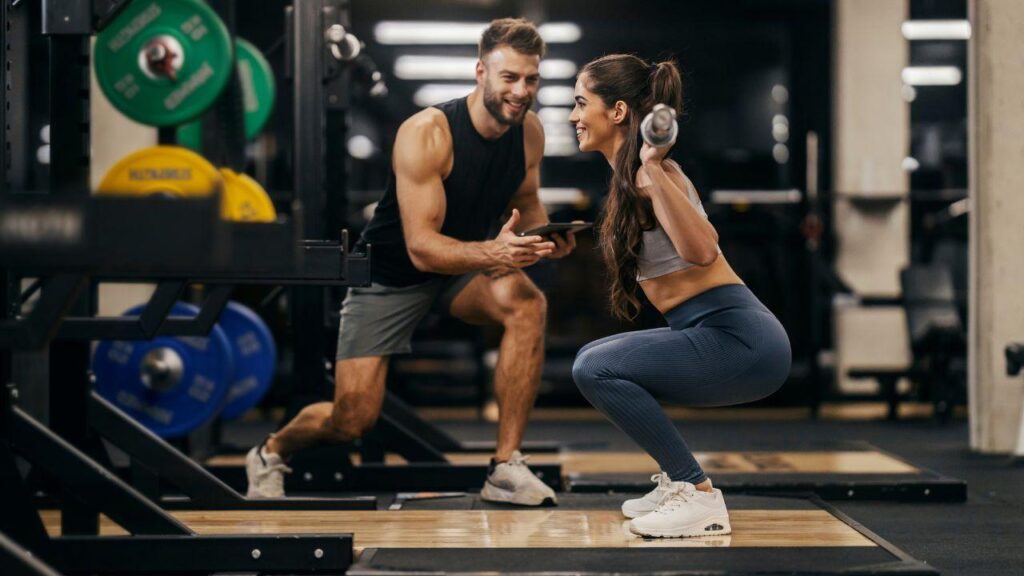Mulher fazendo agachamento com homem ao lado.