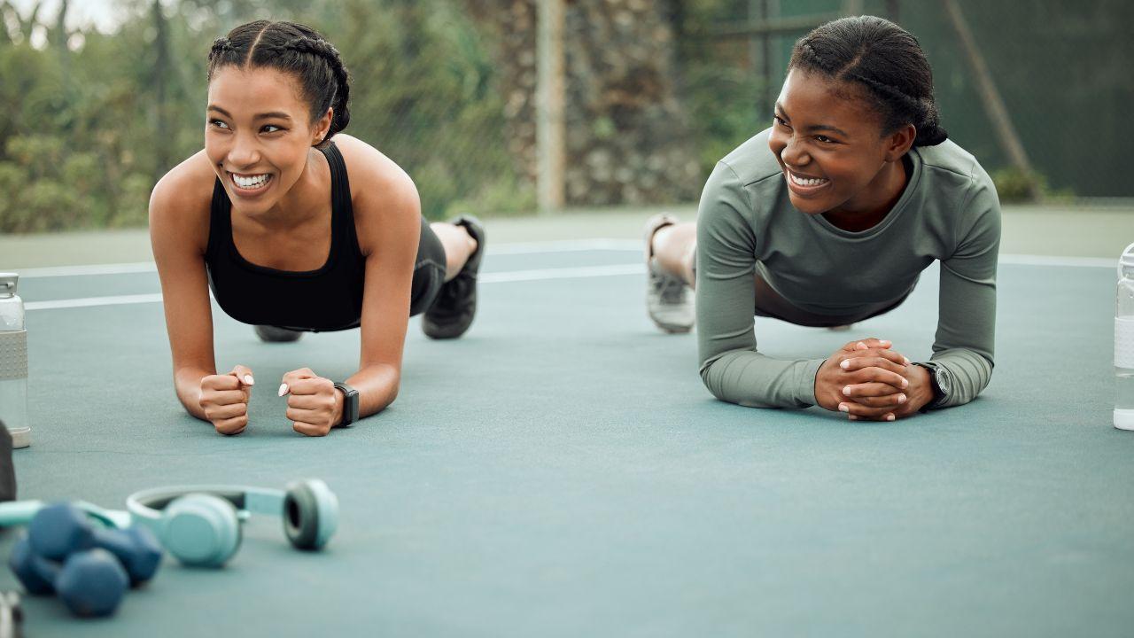 Duas mulheres negras fazendo prancha ao ar livre em um colchonete.