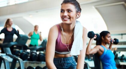 Mulher na academia descansando sentada no banco sorrindo.