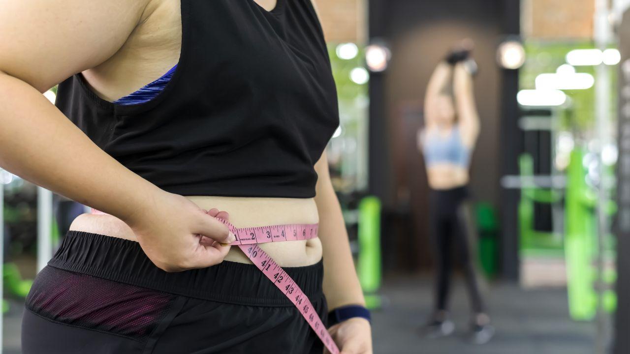 Pessoa medindo a circunferência da barriga com fita métrica, conceito de perda de gordura abdominal.