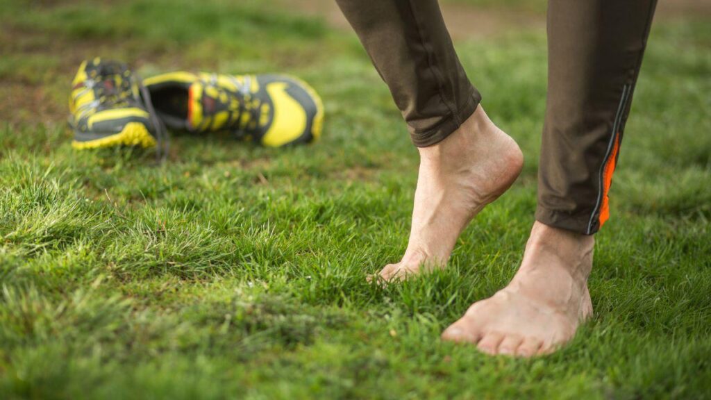 Imagem de uma pessoa descalça na grama com os tênis de exercícios atrás de si