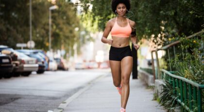 Mulher negra correndo numa rua usando blusa rosa e short preto.