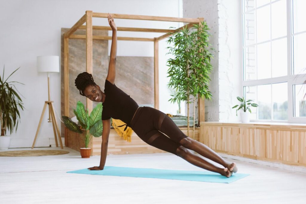 Mulher negra fazendo prancha lateral em um colchonete no chão.