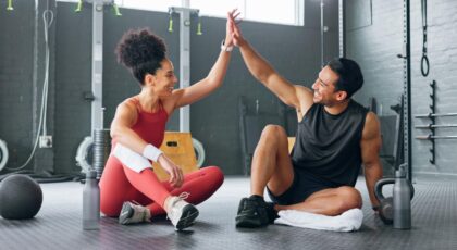 Mulher e homem sentados no chão da academia.