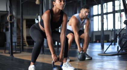 Mulher e homem fazendo exercício na academia, levantando peso.