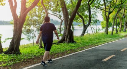 Foto mostra homem caminhando em uma rua bem arborizada.