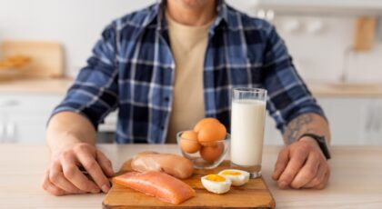 Foto mostra homem sentado na mesa com um prato com ovos, leite e peito de frango na frente.