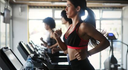 Foto mostra mulher correndo na esteira na academia.